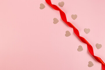 Top view of red ribbon and pink glitter hearts on pink background. Valentine's day, love. Shiny rolled fabric, silk and satin material. Copy space, flat lay.