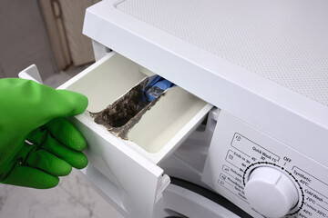 Plumber in gloves inspection of dirty, clogged washing machine. Dirt and mold in open the detergent...