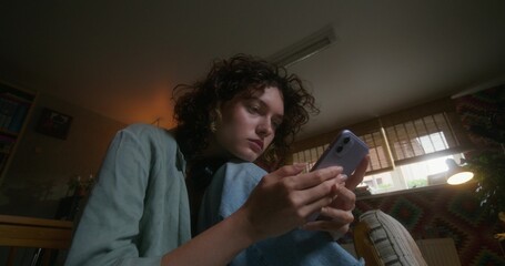 A young woman uses a mobile phone while sitting on a bed at home with a depressed look
