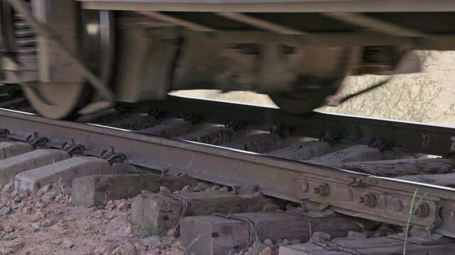 A closeup view of train wheels moving on old bending railroad tracks with old wooden sleepers section at sunny summer day
