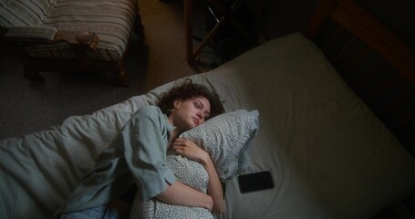 A woman is crying and hugging a pillow lying in bed at home. The mascara is smeared under the eyes. The mobile phone is on her bed