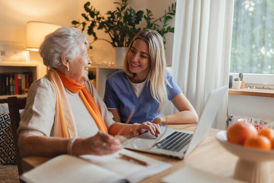 Social worker helping elderly lady with managing her finances, teaching her to use online banking on laptop.