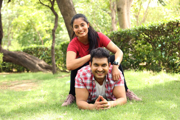 Indian happy young couple embracing, holding hands and looking at camera at park. Portrait of happy couple spending leisure time at park summer day outdoors