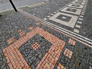 ripples pattern from mosaic cubes on black rough pavement. squares and dashed lines. promenade in the square with repeating lines of the shape of waves and hearts