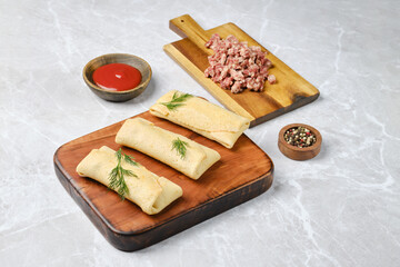 Three rolled crepes filled with seasoned ground meat are arranged on a wooden board