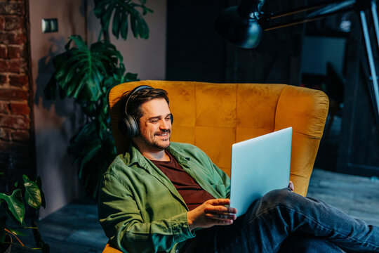 Smiling man with wireless headphones using laptop at home