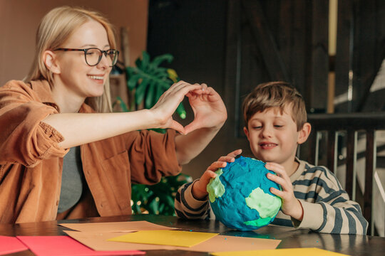 Mother making heart shape with son sculpting clay Earth at home