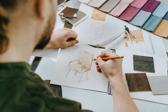 Furniture designer drawing chair on book with pencil at desk in office