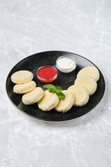 A black plate with curd cheese rounds alongside a strawberry jam and a sour cream