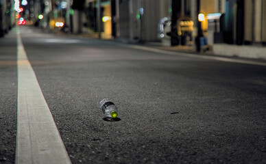 A single discarded plastic bottle lying on an empty street at night in a quiet area of Tokyo, Japan