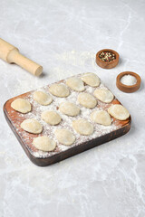 Freshly made dumplings ready for cooking on a wooden board with a rolling pin