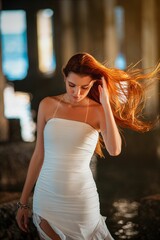 Woman in white dress under pier with sunlight.