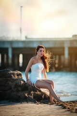 Woman in white dress by the beach at sunset.