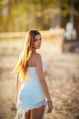 Woman in white dress on sunlit beach.