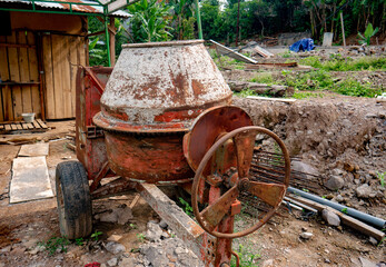 The cement mixer machine is parked at the construction site, there is a lot of rust on its body