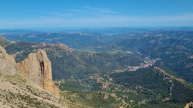 Panning shot from the top of a mountain pass in the Tell Atlas region of Kabylie, Algeria, offering a wide view of the green, hilly landscape stretching to the horizon on a sunny day