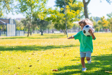 Smiling child running in a green park while holding a soccer ball, enjoying a sunny day of outdoor play and exercise, promoting children's health, happiness, and physical activity