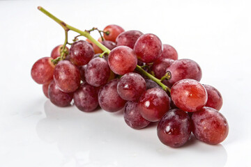 Fototapeta premium Red Grapes on Stem: A vibrant bunch of red grapes, glistening with dew, hangs from its stem, showcasing its plump, juicy berries. The image is perfect for showcasing fresh produce, healthy eating.