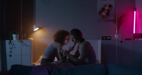 Naklejka premium A man and a woman use mobile phones while sitting on a bed at night. Dark room, home interior