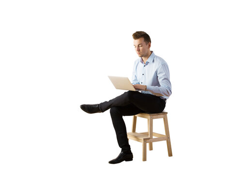 Man in a blue shirt andpants sitting on a wooden stool with a laptop, isolated on white background. Concept of work, business, or remote job