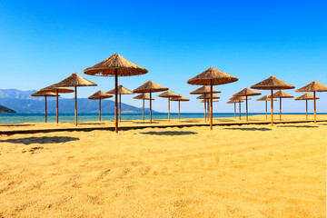 Row of wooden umbrellas at sandy beach, sea