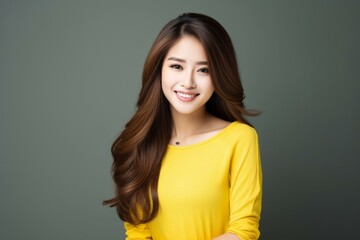 Fototapeta premium Portrait of beautiful smiling asian woman with long brown hair, perfect white teeth and yellow shirt on gray background