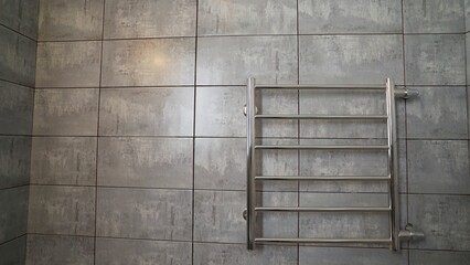 Chrome heated towel rail warmer drying rack hanging on grey wall tiles in bathroom