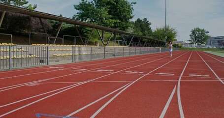Obraz premium A woman in sports clothes and with earbuds in her ears runs at speed at the city stadium on a summer day