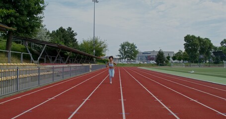 Obraz premium A woman in sports clothes and with earphones in her ears runs at the stadium on a summer day