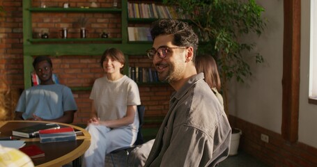 A group of young people are smiling and talking while sitting around a table. They study the Bible...