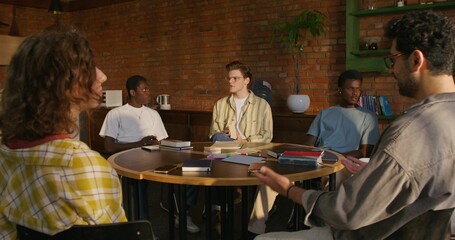 Bible Study Group. Young people talk in pairs while sitting at a table indoors. The books are on...