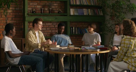 A man is talking to his friends while sitting at a table indoors. He opens the Bible. Bible Study Club
