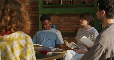Young people of different nationalities read the Bible while sitting at a table indoors. They are...