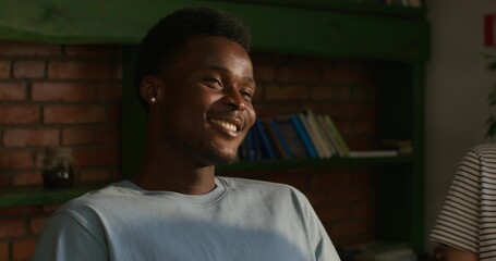 A man is smiling and talking to his friends while sitting at a table indoors. Daylight