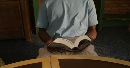 A man is flipping through the Bible while sitting indoors. The video moves from his hands to his...