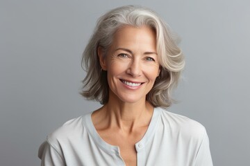Portrait of a beautiful smiling senior woman with gray hair, radiating happiness and confidence against a gray background