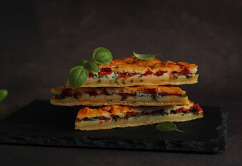 slices of pie with tomatoes and basil cut in rows on a dark background