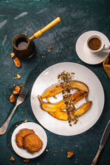 Bananas flambe on a white plate with nuts and chocolate on a table with coffee and a cezve on a dark background with a knife and fork. Top view. Restaurant serving dessert