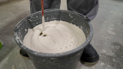 Construction worker mixing plaster in bucket with mixing paddle
