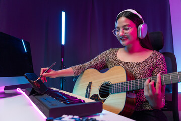 Professional Women Musician composing a song with acoustic guitar, piano keyboard and condenser...