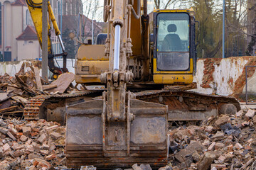 Fototapeta premium demolition of a residential building in the city center from red old brick using a hydraulic excavator. lying brick on the ground. pile of dirt. signs and signs of construction and road works at sunri