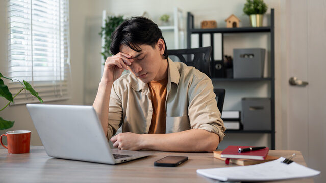 A serious, stressed Asian businessman is concerned about the deadline, suffering from a headache.