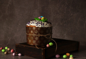 Easter cupcake with icing on wooden box on dark background with colored eggs