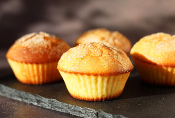 Dessert muffins with sugar crust on a black stand on a dark background