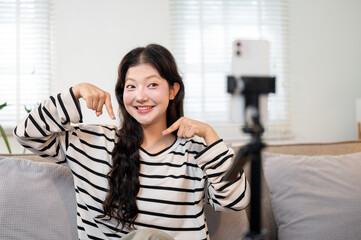A cheerful Asian female influencer is recording a video reviewing a clothing brand.