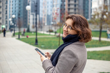 Fototapeta premium Portrait of young woman strolling through city street with phone.