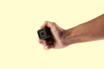 Male hand holding an action camera isolated on yellow background side view