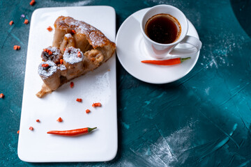 Tarte Tatin a French banana dessert, a slice of pie on a white plate with freeze-dried raspberries and hot chili peppers with a cup of strong coffee on a dark green background. Space for text,