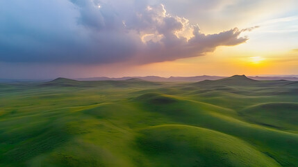 Obraz premium Aerial view of green hills and cloudy sky at sunset in spring, panoramic landscape from a drone with summer nature, sunlight on the grassy mountains
