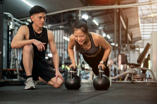 A determined Asian female client is being trained by a professional fitness trainer in the gym.